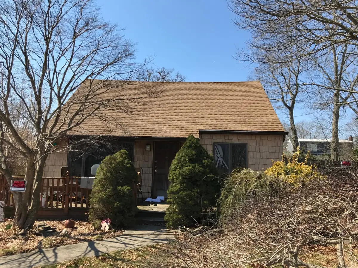 Selling a rental property in Shirley: shingled cape behind overgrown front shrubs
