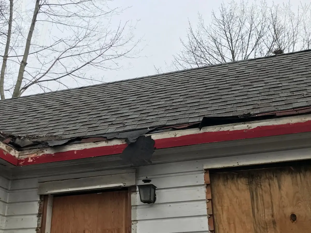 Selling a storm-damaged house in Shirley: torn roof edge above boarded up windows